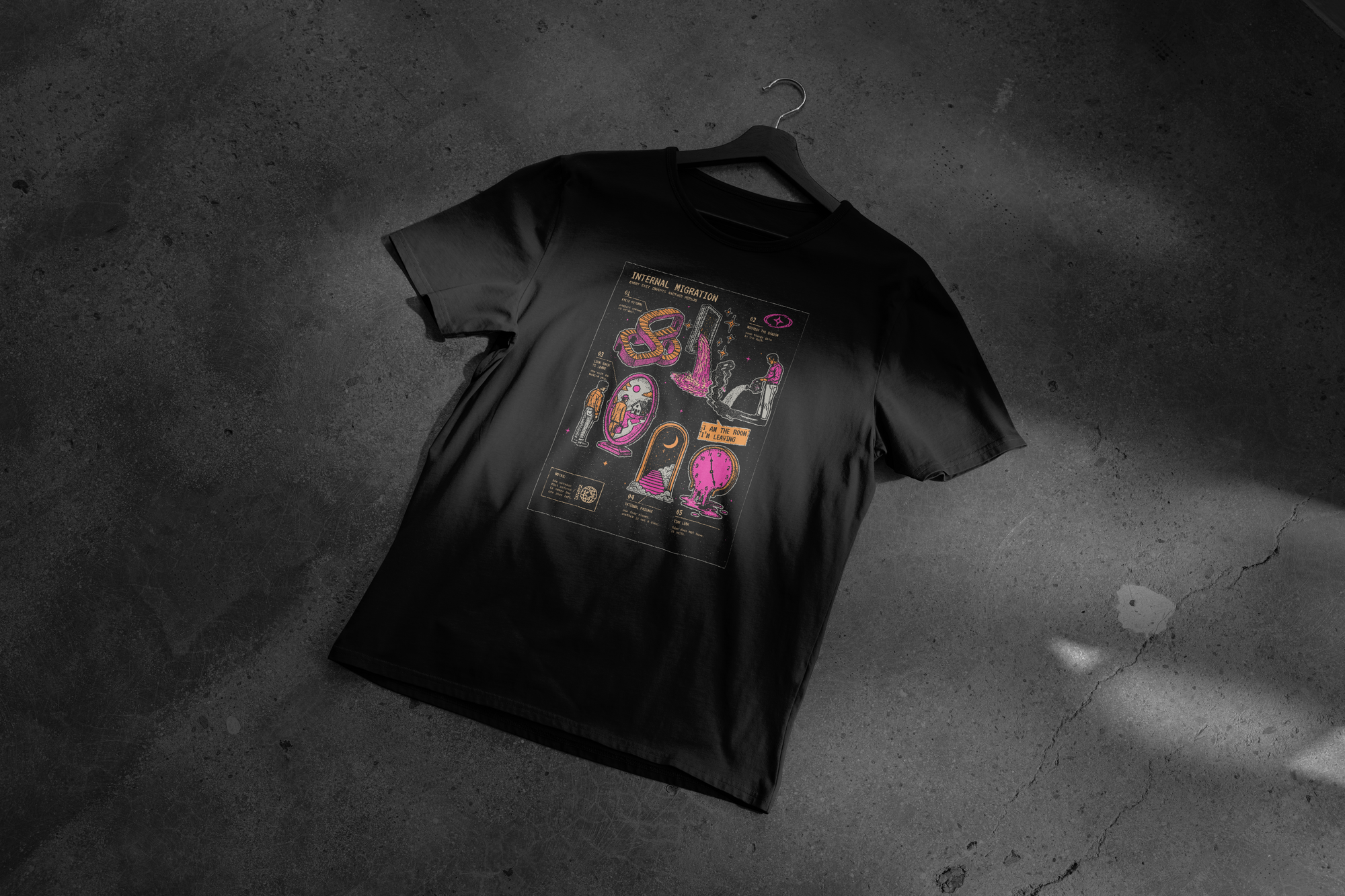 Black heavyweight garment-dyed T-shirt mockup featuring the “INTERNAL MIGRATION” graphic collage with distressed illustrations, pixel-inspired typography, stars, diagrams, and fragmented symbolic imagery on a dark background.